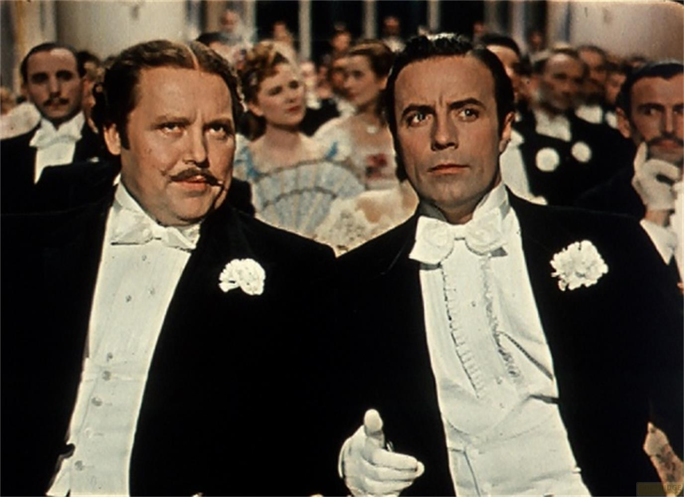 Due uomini in smoking con papillon e fiore all'occhiello siedono tra il pubblico.