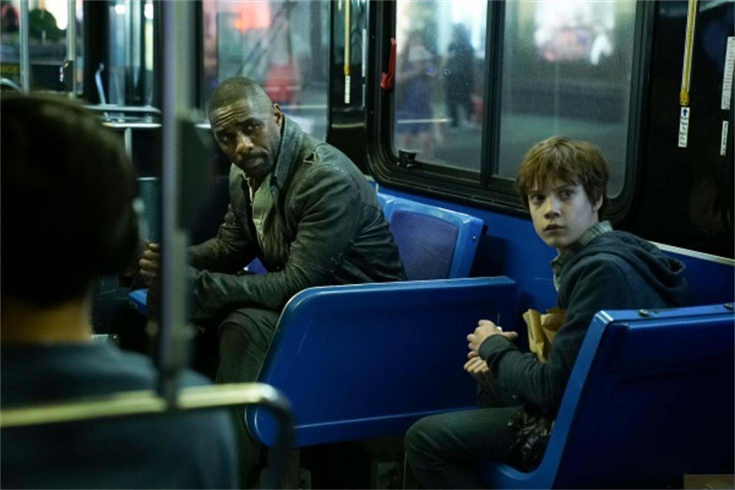 Deux hommes assis dans un bus. L'un est noir avec une veste en cuir, l'autre est un jeune homme blanc.