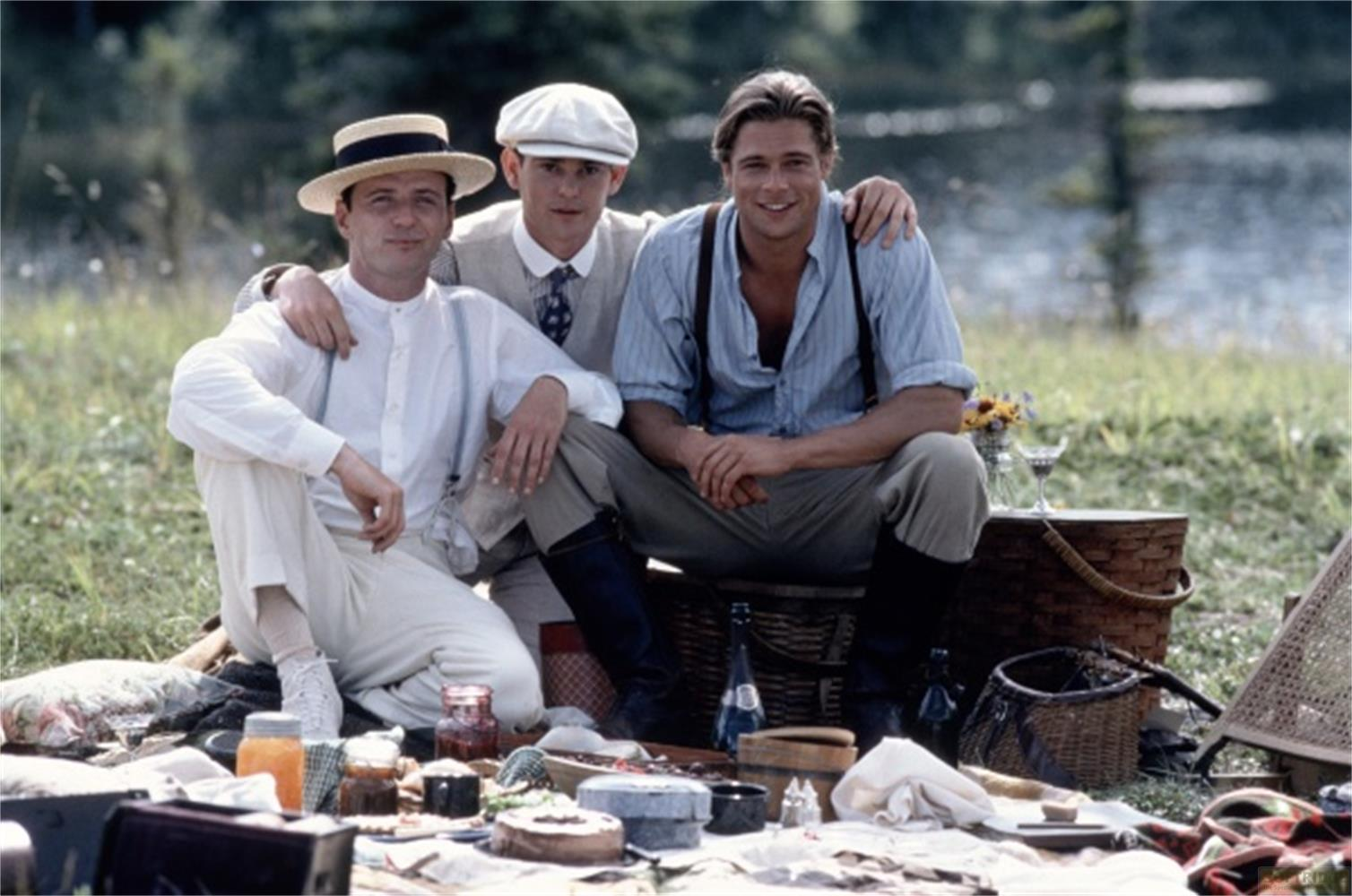 Tre uomini in abiti vintage fanno un picnic in riva al lago. Uno indossa un cappello di paglia.