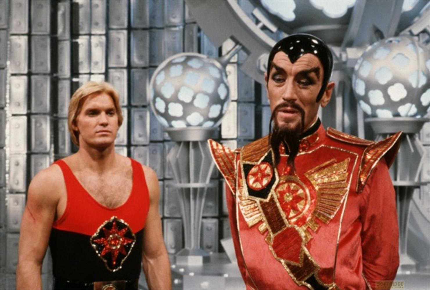 Un uomo biondo indossa una canottiera rossa e nera. Un uomo dai capelli scuri indossa una veste rossa e oro.