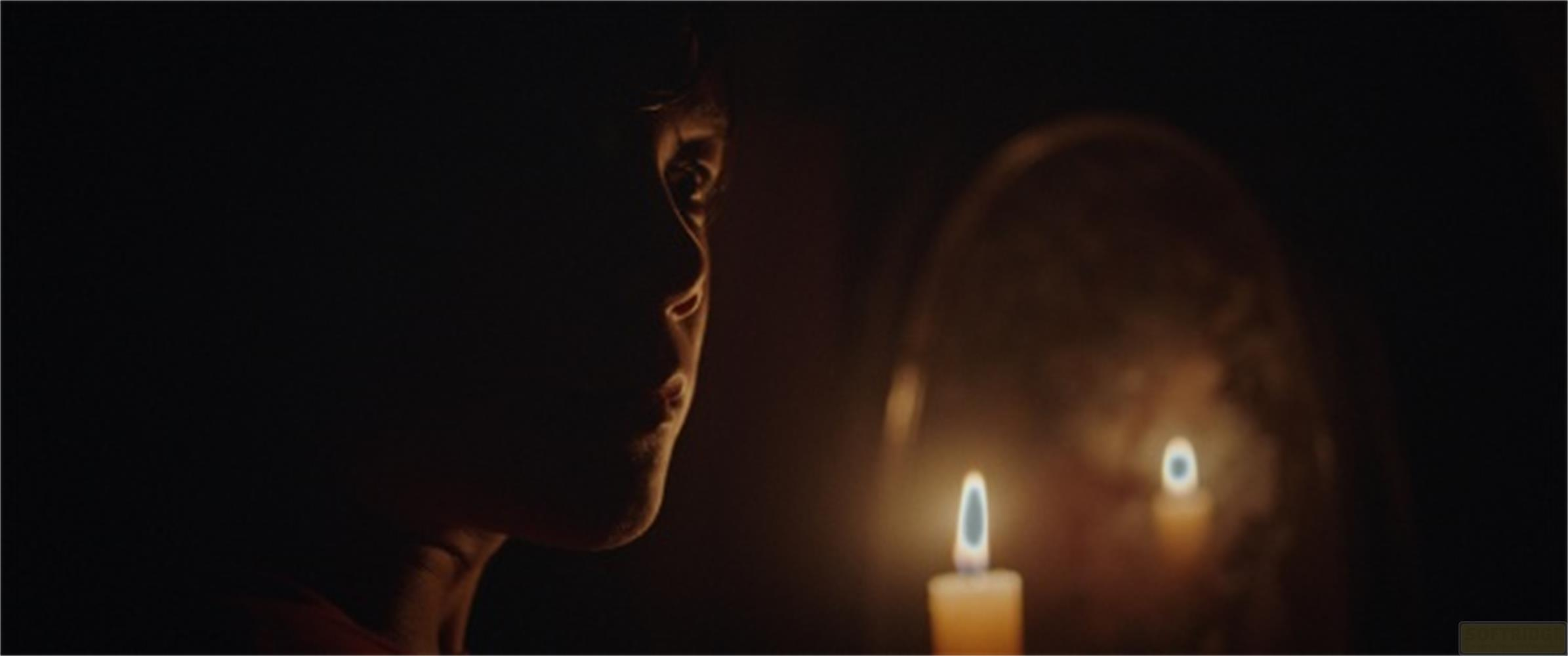 Un bambino guarda il riflesso di una candela alla luce di candela.