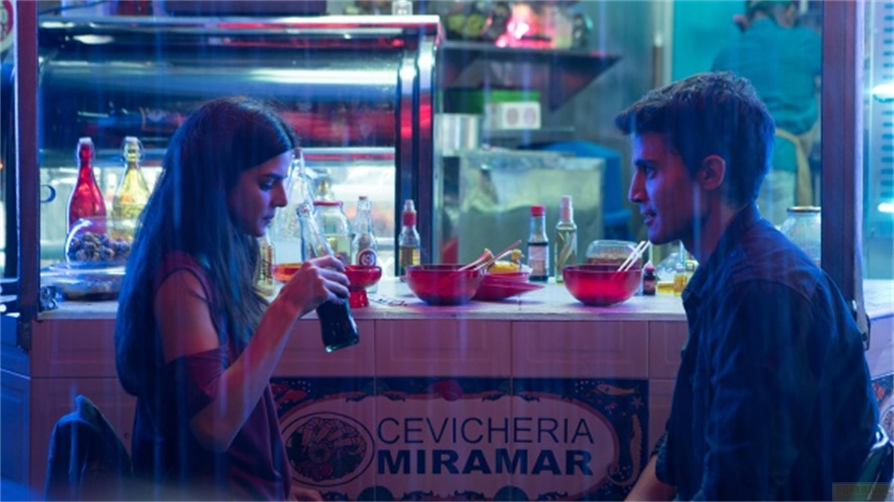 Un homme et une femme assis à un bar. La femme boit dans une bouteille.