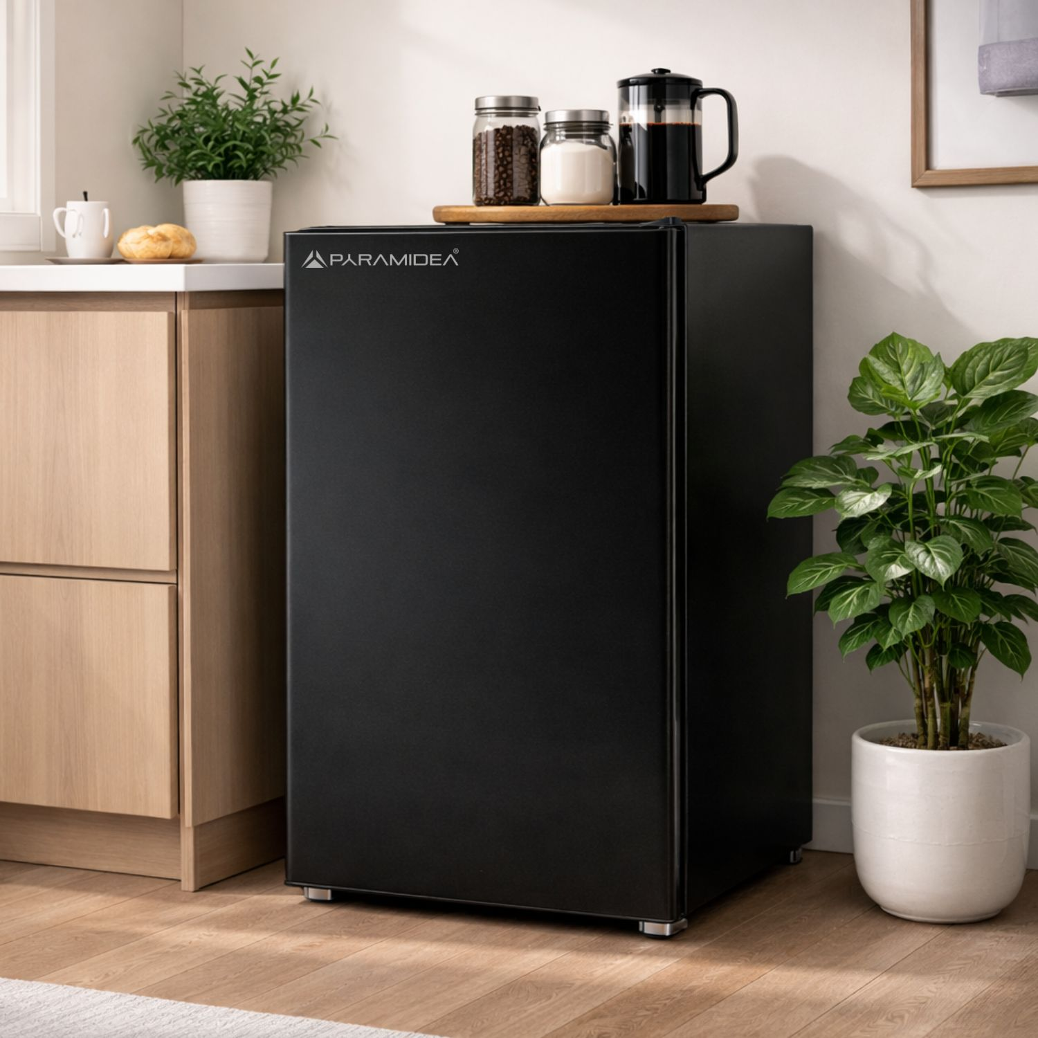 Un mini-frigo nero accanto ad armadi in legno e una pianta.