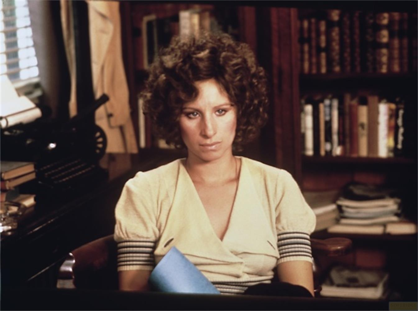 Une femme aux cheveux bouclés est assise devant une bibliothèque.