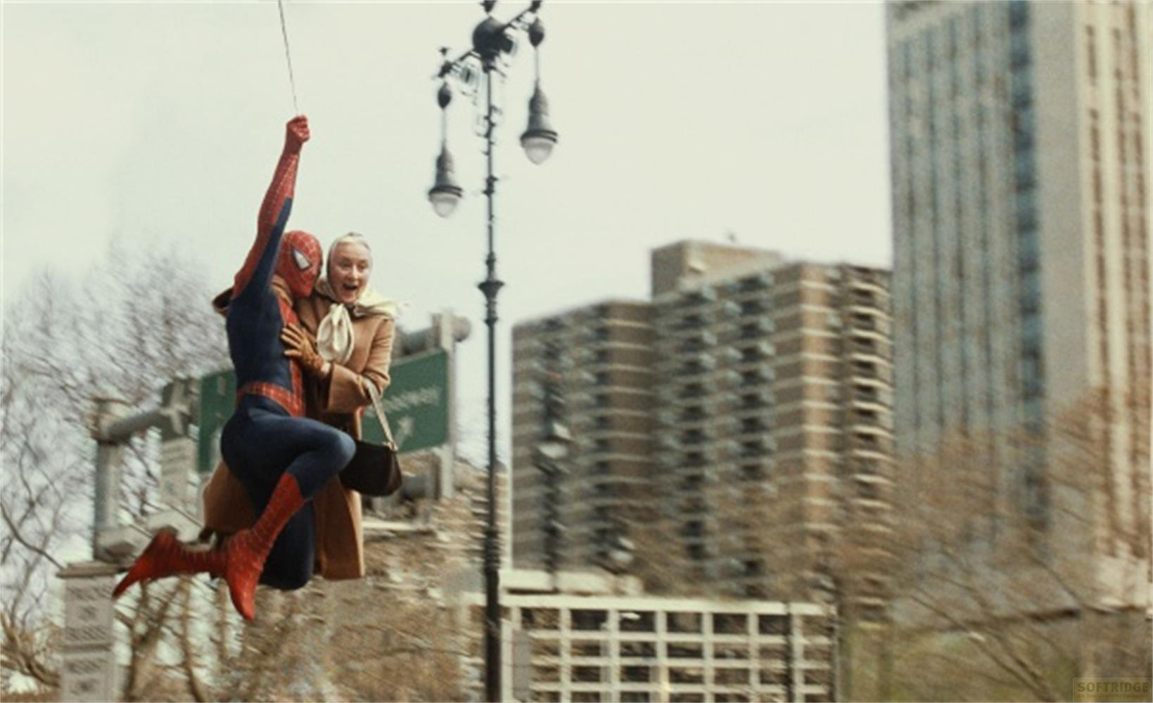 Spider-Man se balance avec une femme qui le tient, des immeubles en arrière-plan.