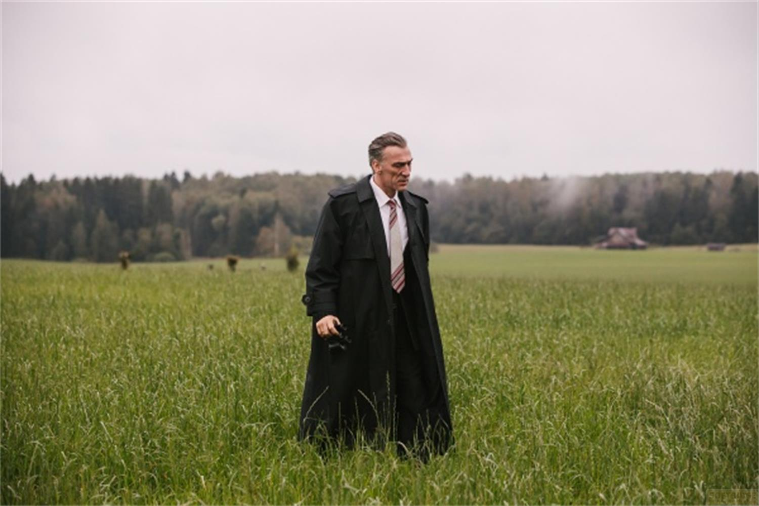 Un uomo in un lungo cappotto nero si trova in un campo verde.