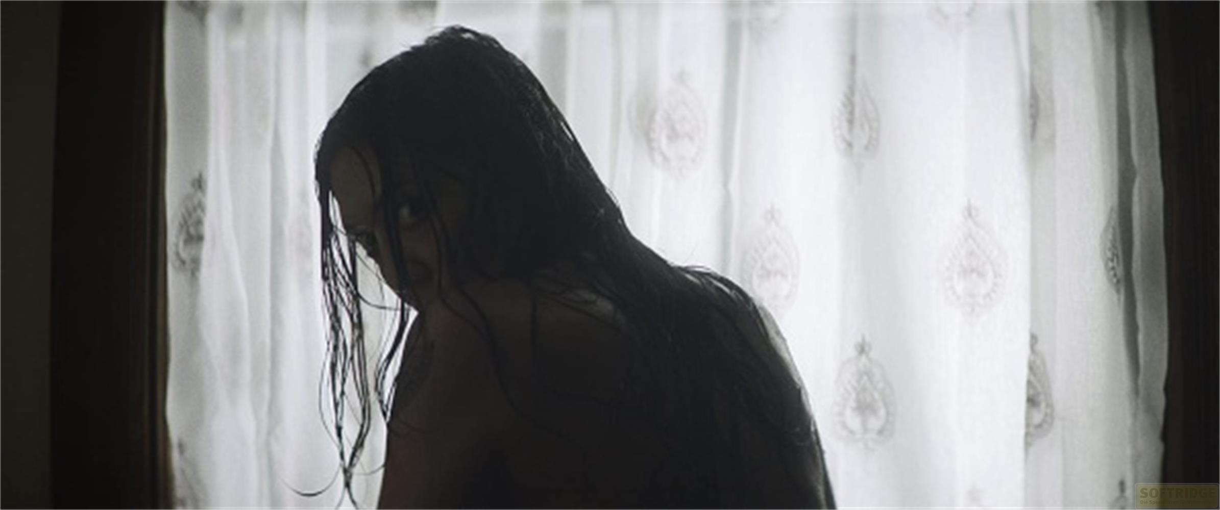 Una donna con lunghi capelli scuri si volta all'indietro, davanti a una tenda fantasia.