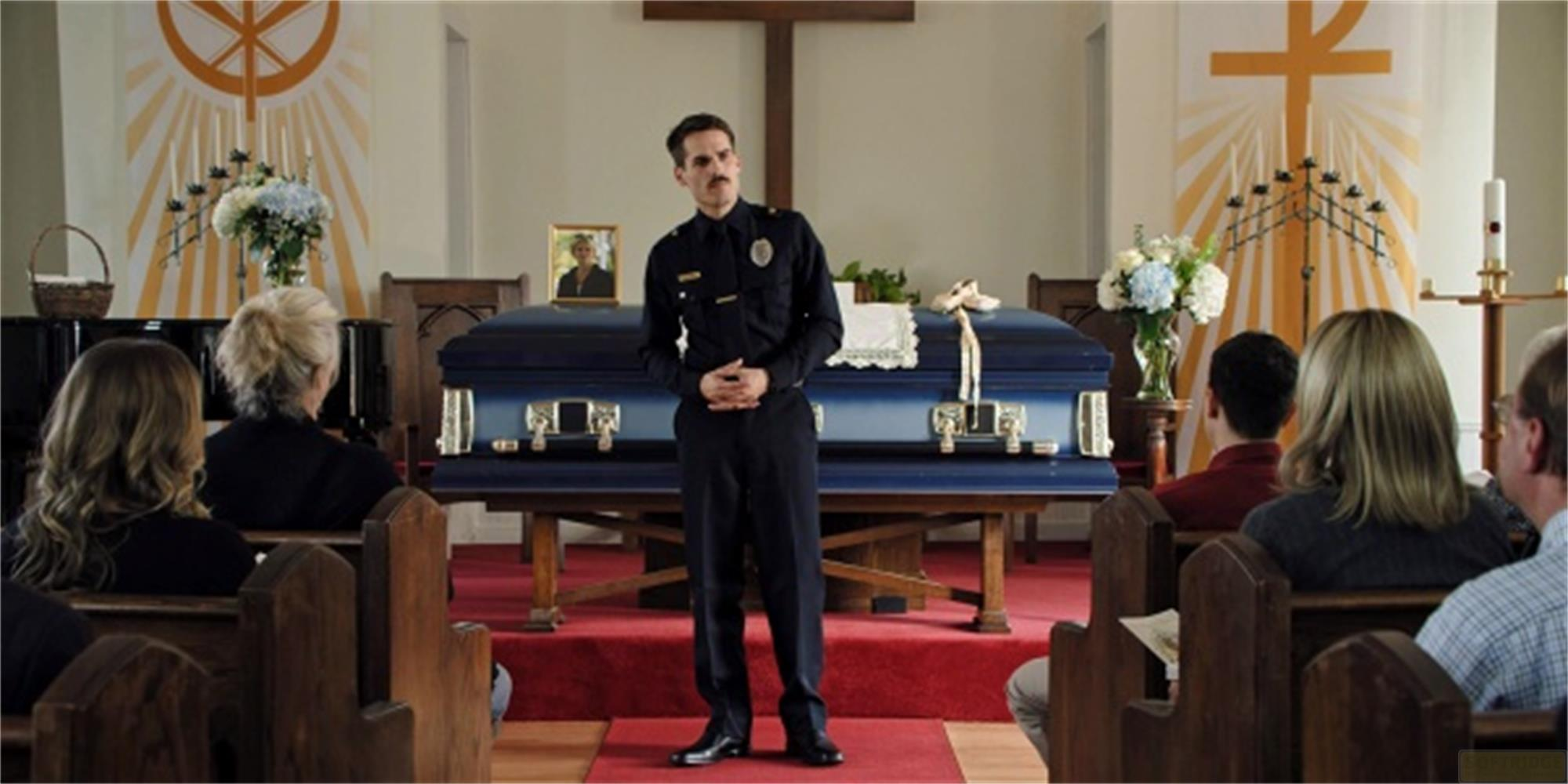 Un poliziotto sta davanti a una bara in una chiesa mentre i dolenti sono seduti.