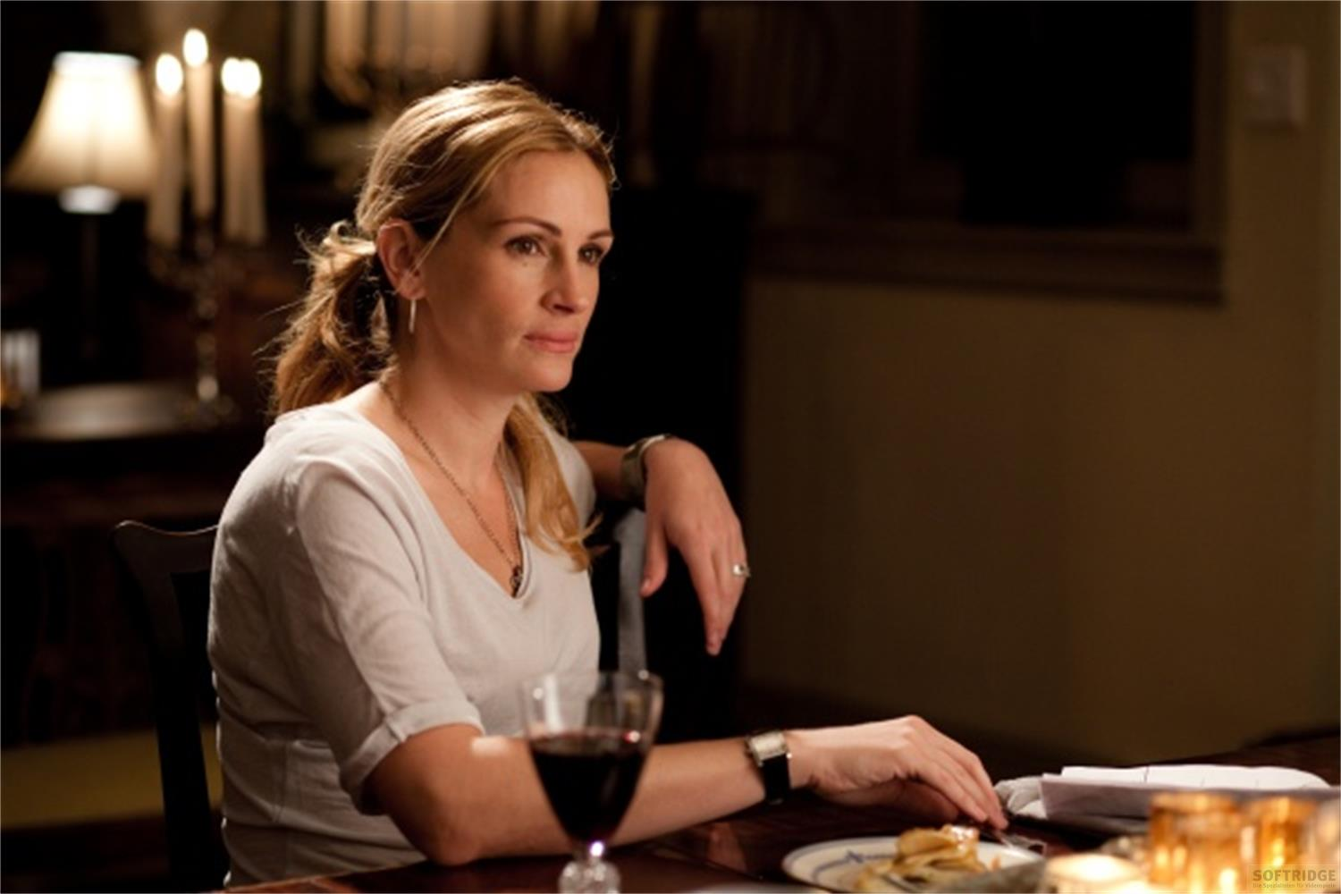 Une femme assise à table, boit du vin et mange.