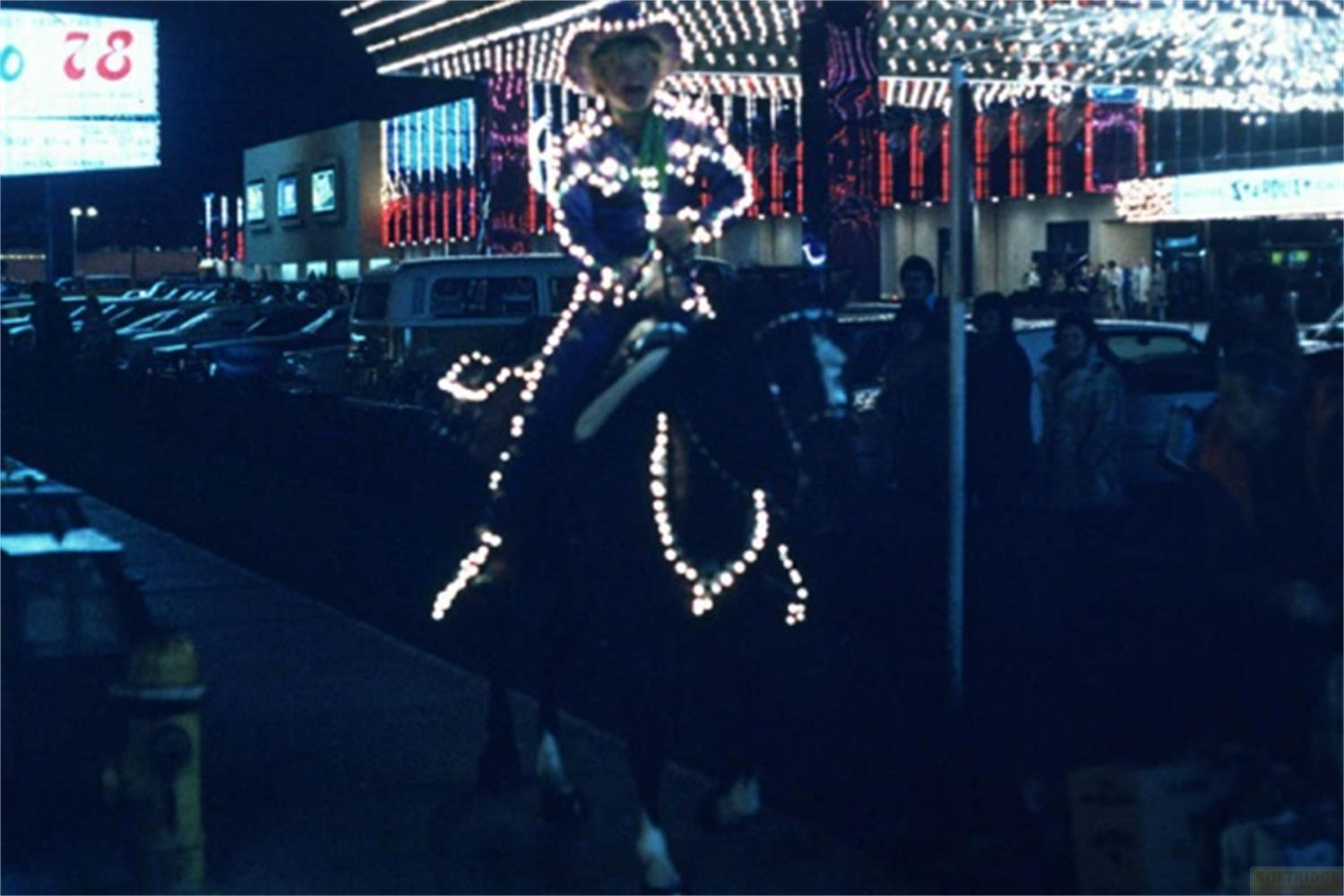 Una persona a cavallo adornata di luci, di fronte a un casinò di notte.