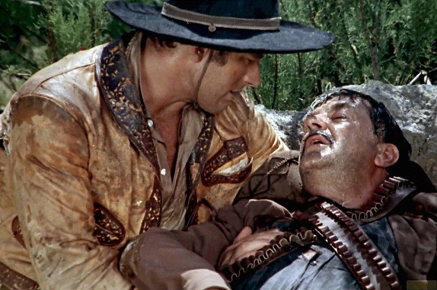 Un uomo con cappello da cowboy si china su un altro uomo sdraiato.