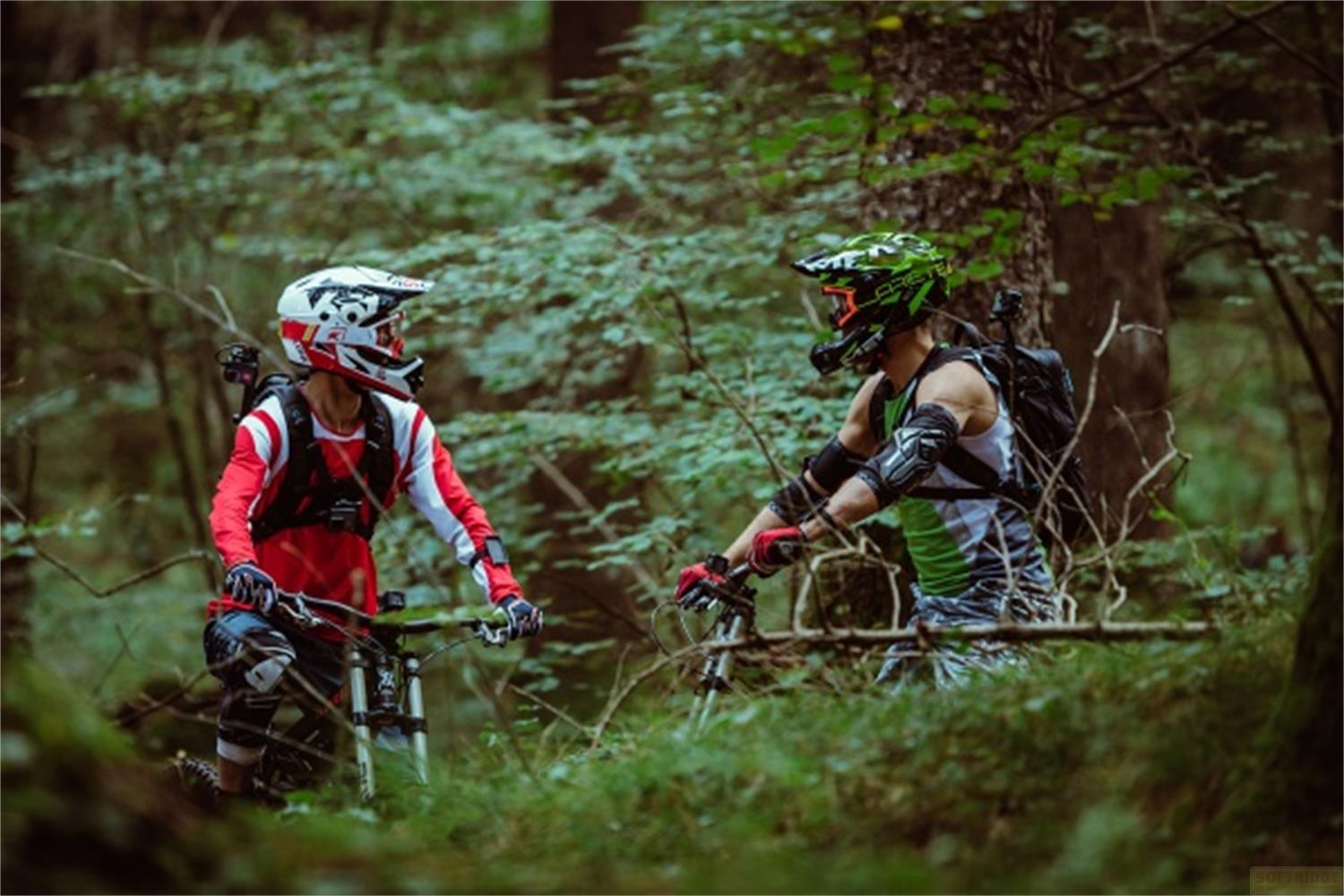Due mountain biker in abbigliamento protettivo completo in una foresta.
