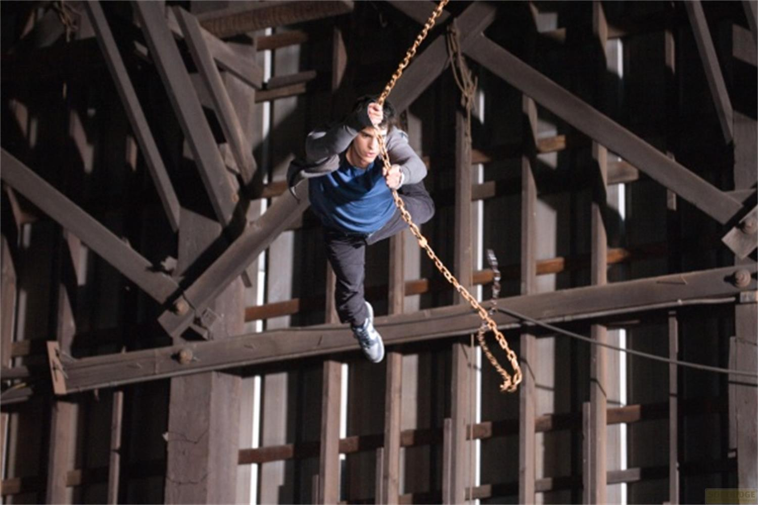 Un uomo si arrampica su una catena all'interno di una struttura di legno.