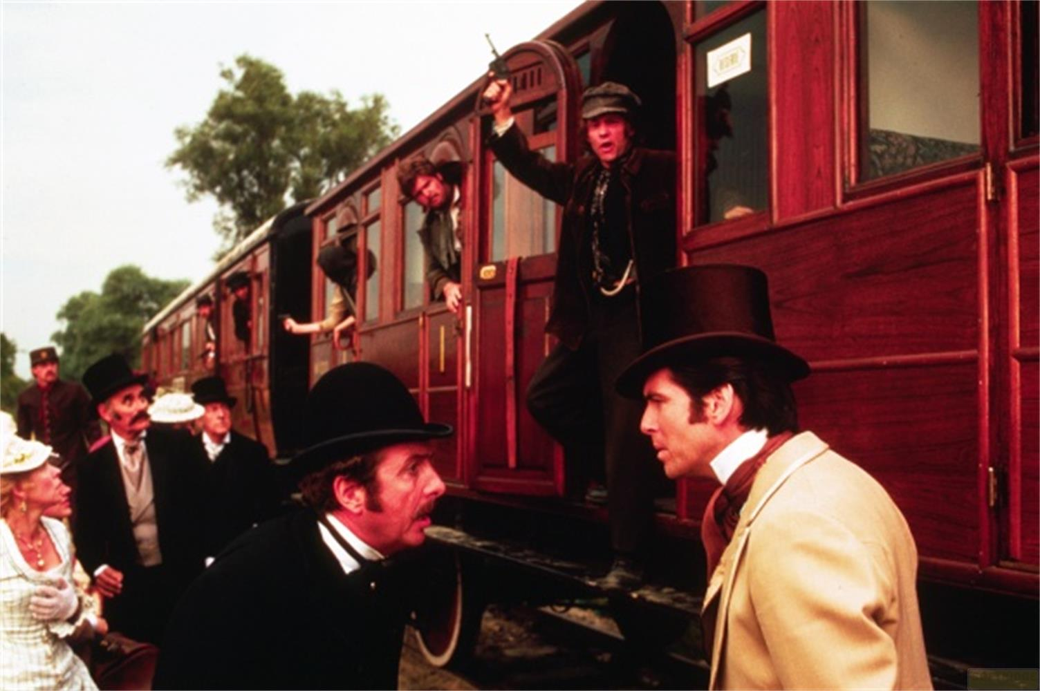 Uomini in abiti vittoriani scendono da un treno rosso.