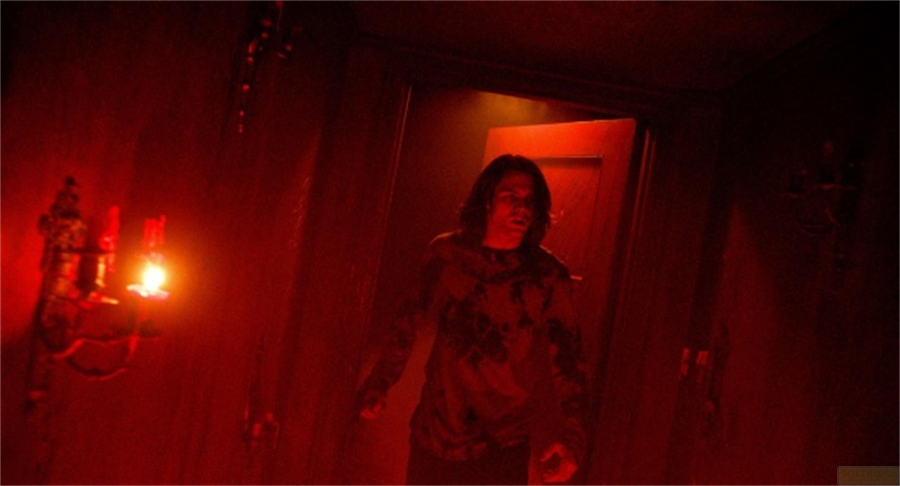 Un uomo dai capelli scuri si trova in una stanza buia illuminata di rosso.