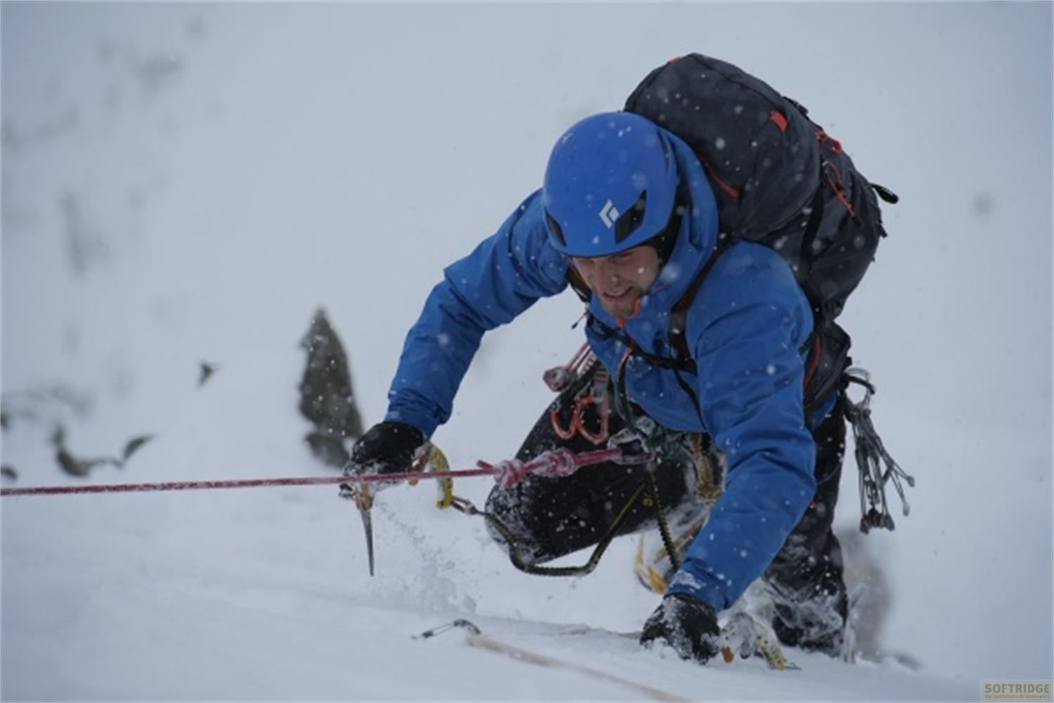Un alpinista in giacca blu sale un pendio innevato, con zaino e corda.