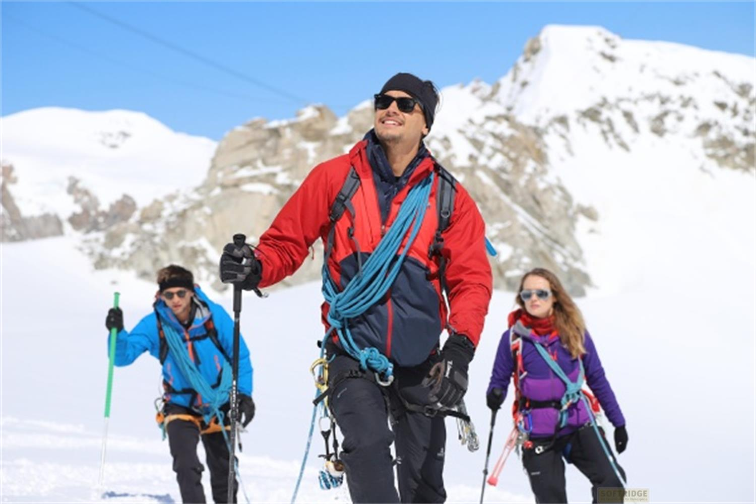 Tre alpinisti in abiti colorati escursionano su un pendio innevato con bastoncini.