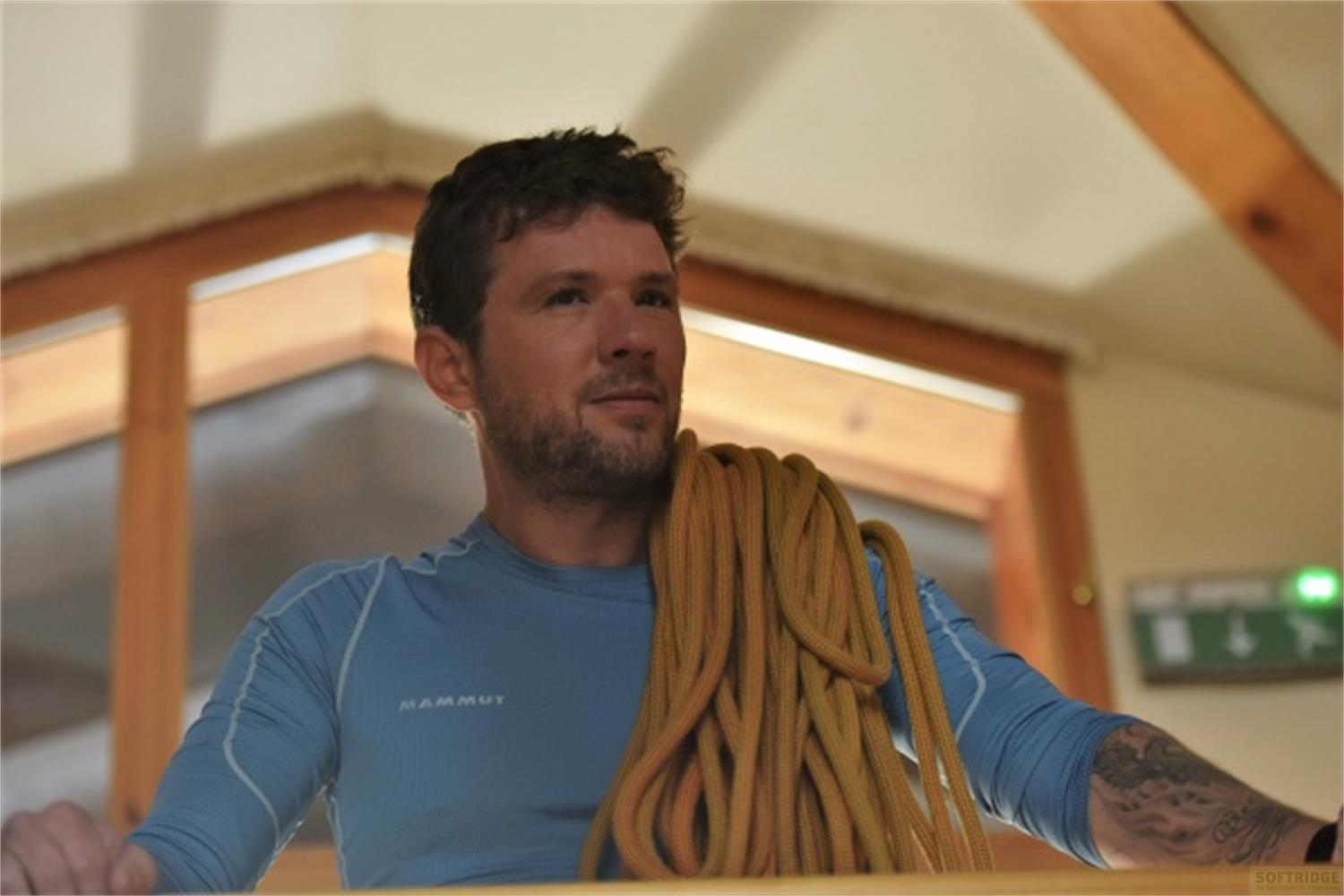 Un uomo con la barba indossa una maglia blu, portando una corda gialla sulla spalla.