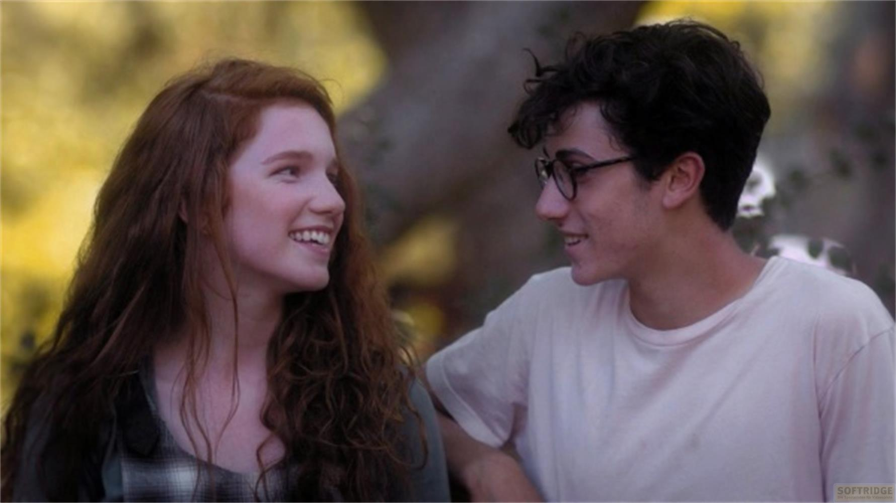 Una giovane donna rossa e un uomo con gli occhiali si sorridono.