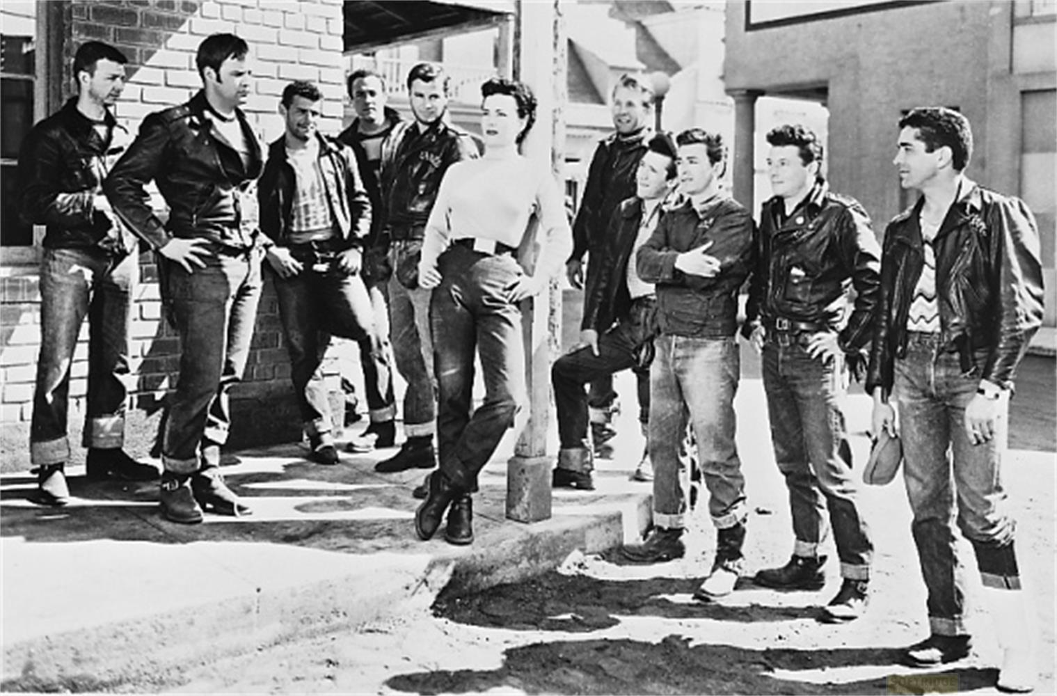 Una donna sta davanti a un gruppo di uomini in giacche di pelle e jeans.