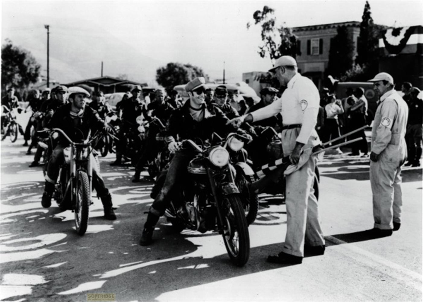 Un gruppo di motociclisti e ufficiali di gara si trova in una strada.