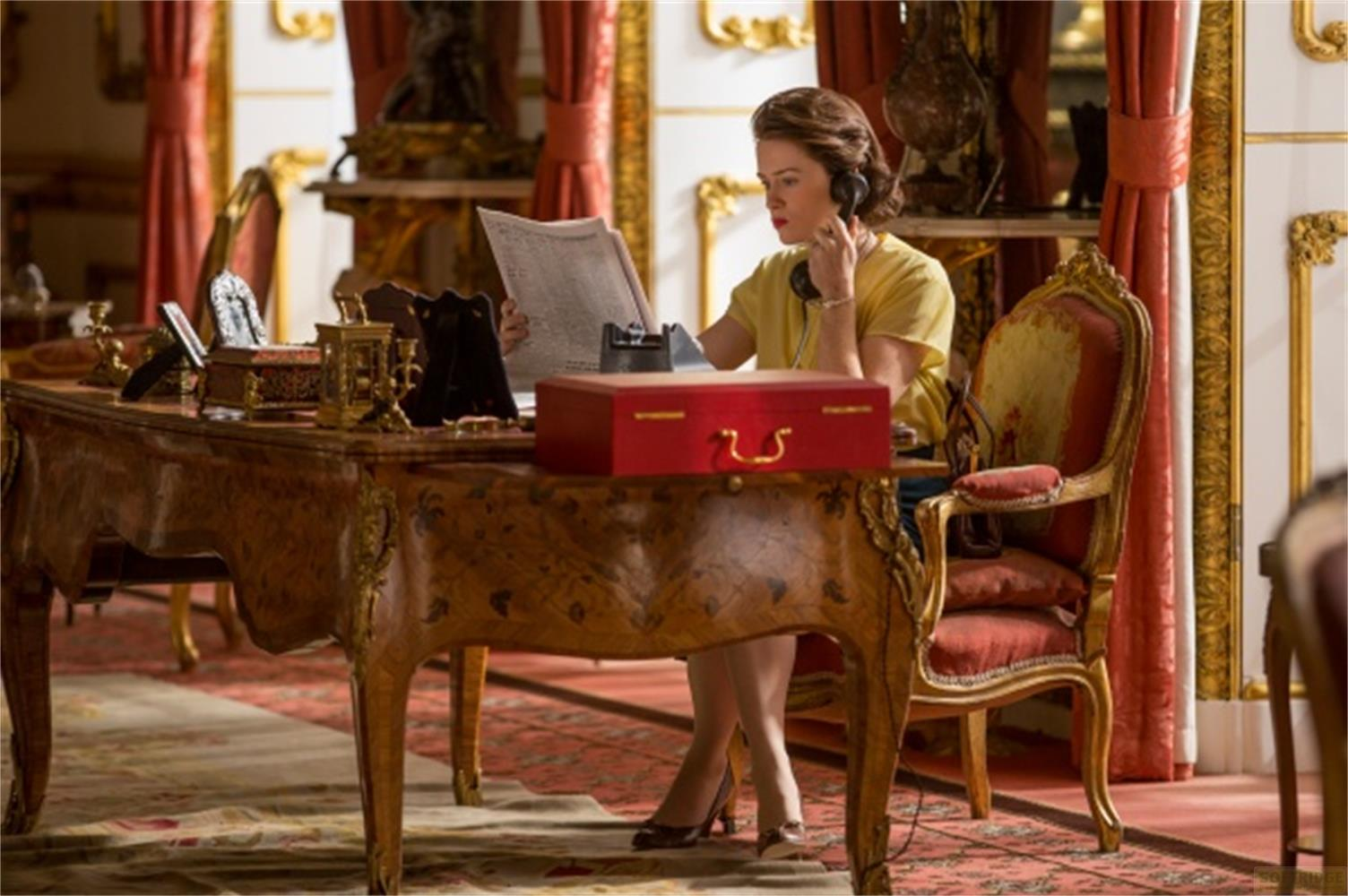Una donna con top giallo è al telefono a una scrivania ornata.