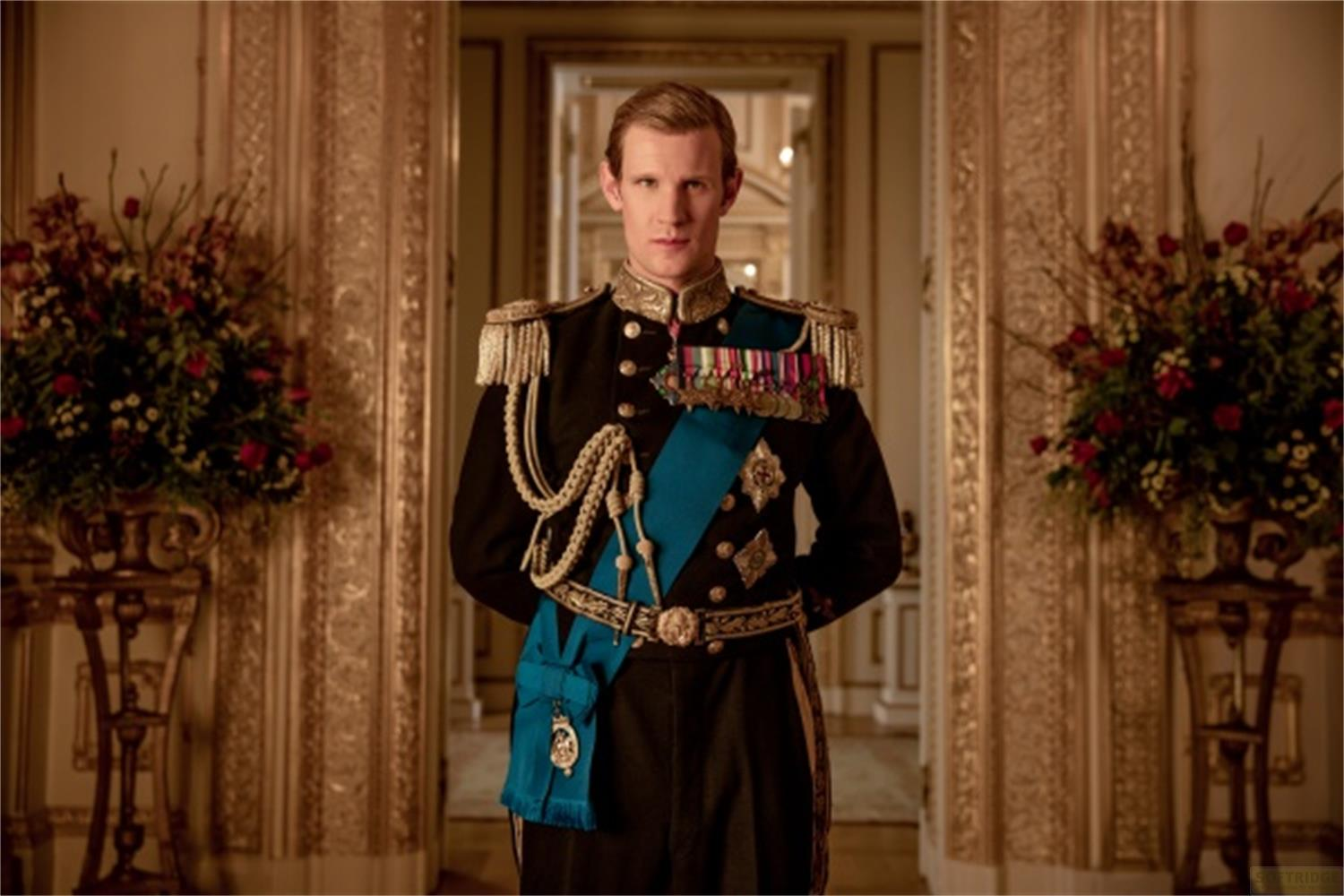 Uomo in uniforme militare con medaglie e fascia blu in una stanza opulenta.