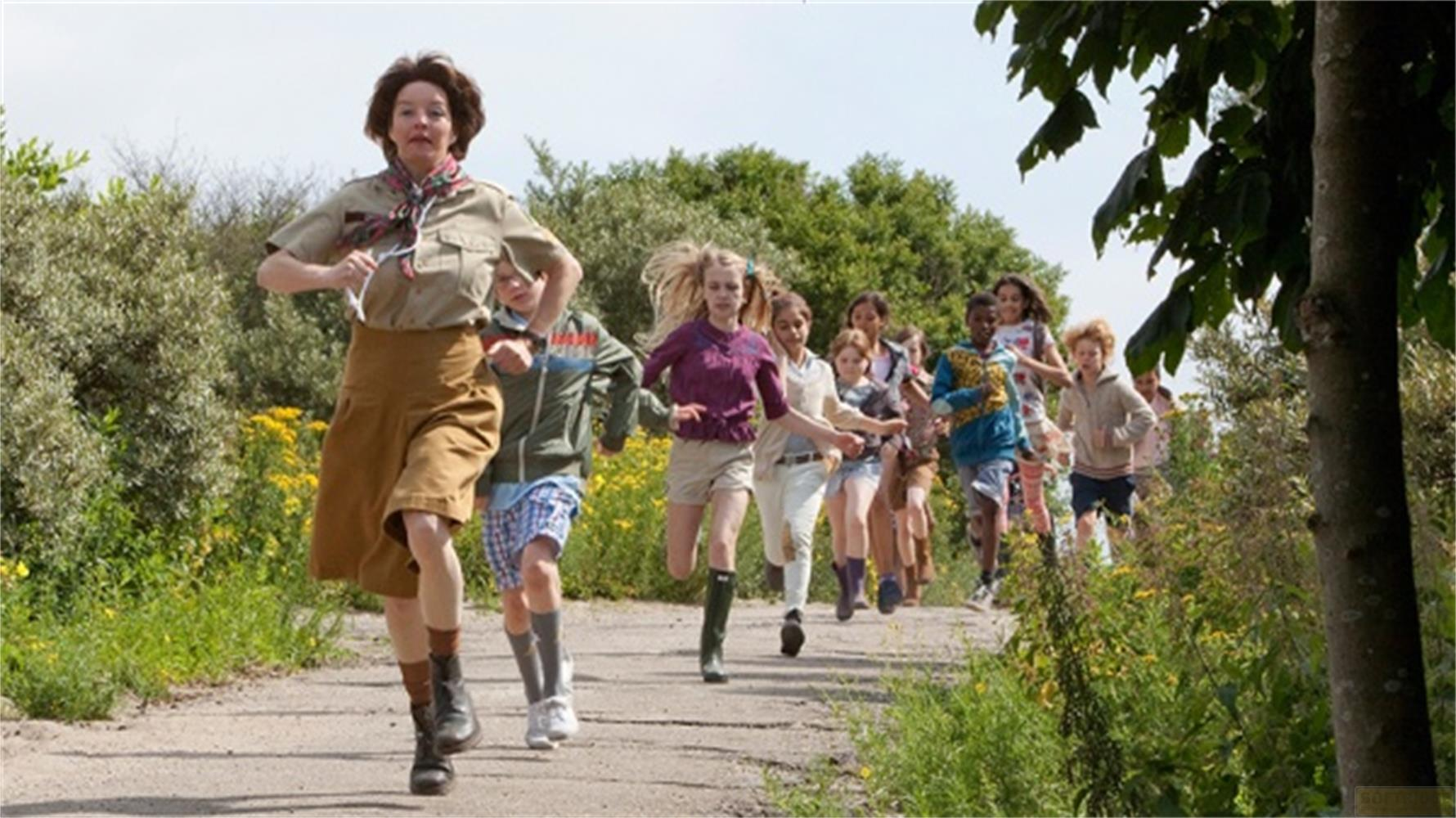 Une femme en uniforme et des enfants courent sur un sentier dans la verdure.