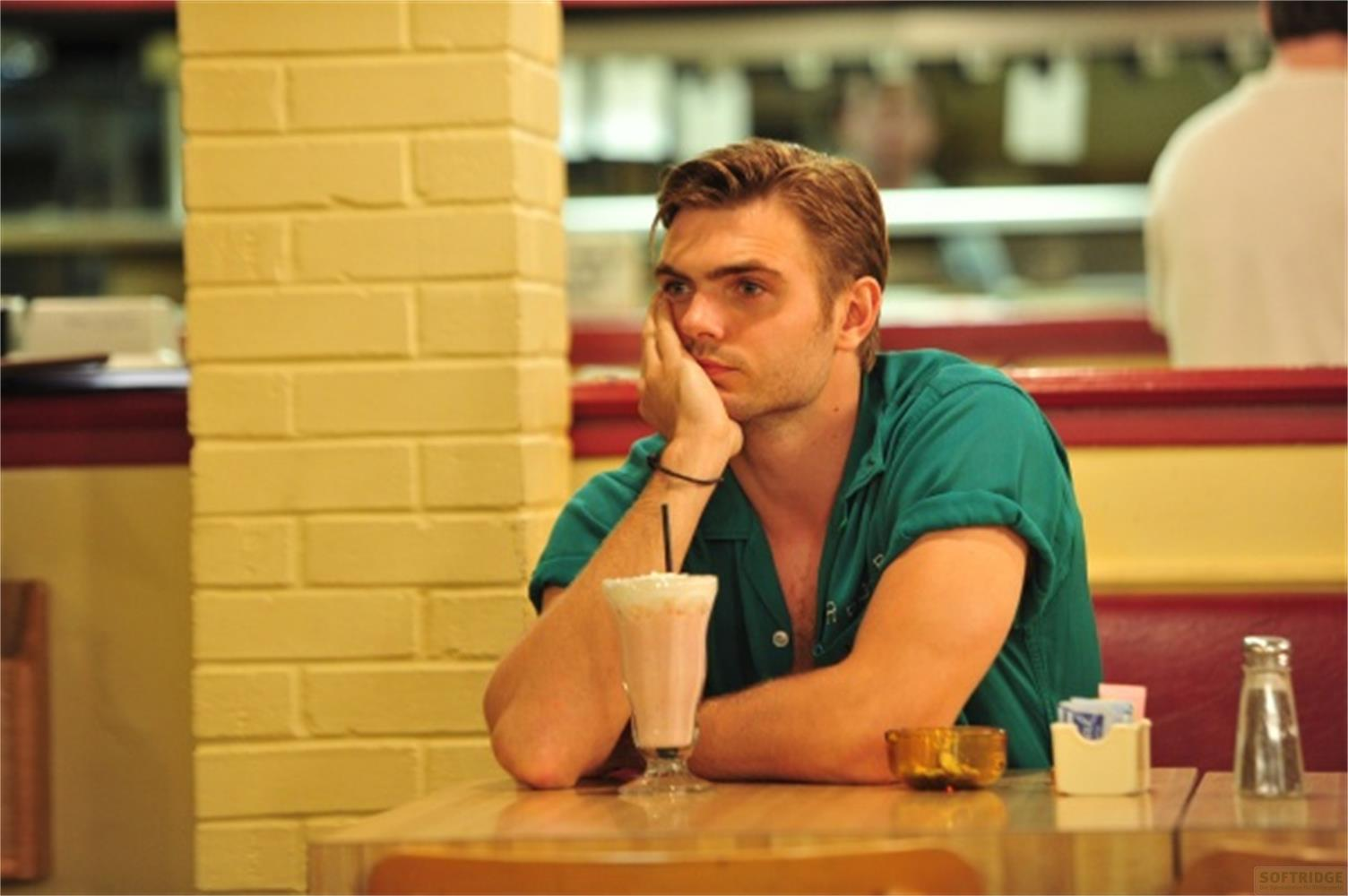 Un uomo con la mano sul mento siede in una tavola calda con un frappè.