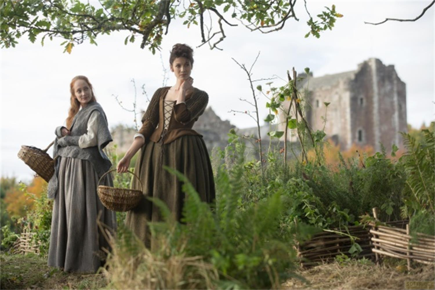 Zwei Frauen in historischen Kleidern stehen im Freien mit einem Schloss im Hintergrund.