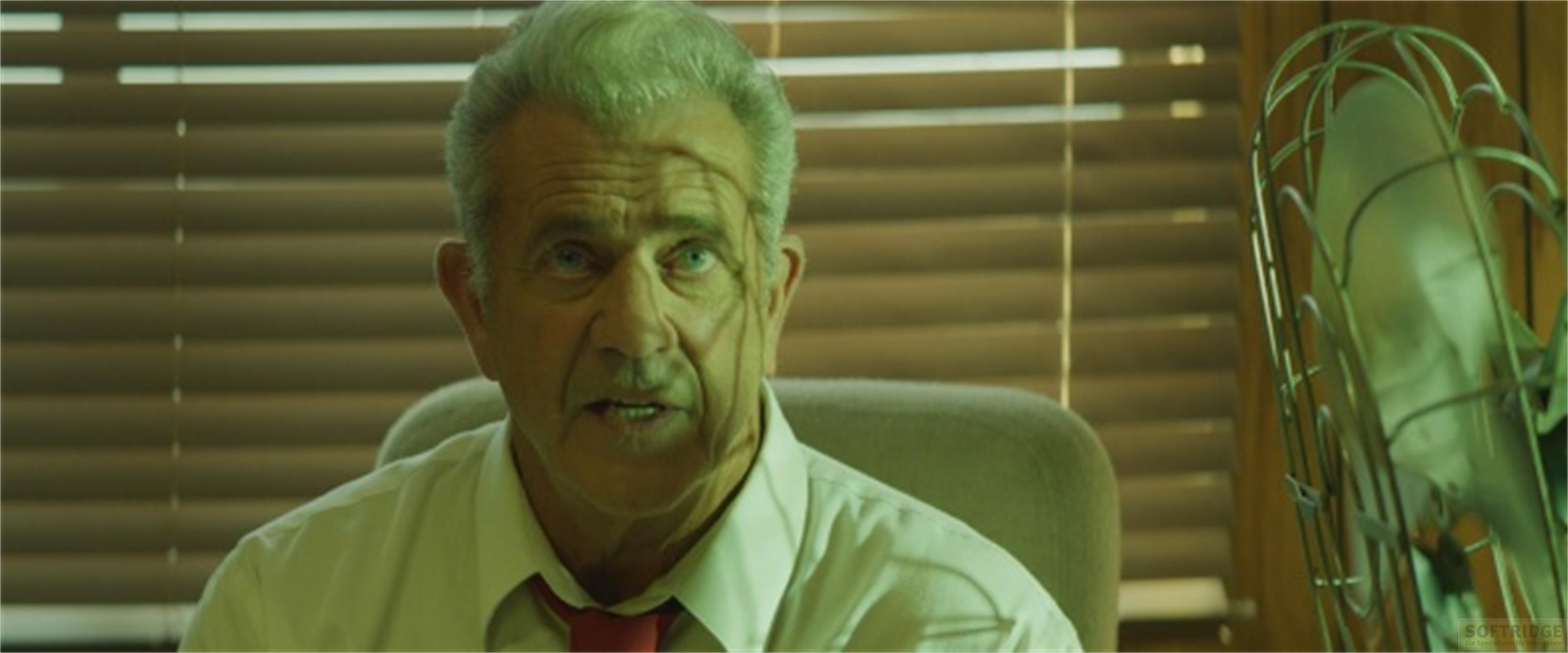 Un uomo con i capelli grigi siede davanti a delle tende e un ventilatore.