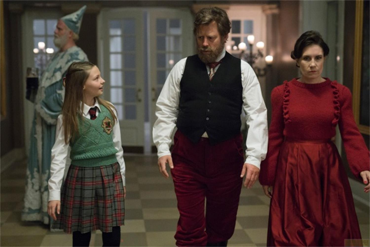 Un homme barbu, une fille en uniforme scolaire et une femme en rouge marchent.