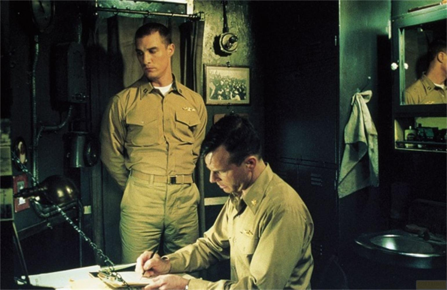 Zwei Männer in Uniform stehen in einem spärlich beleuchteten Raum, einer schreibt.
