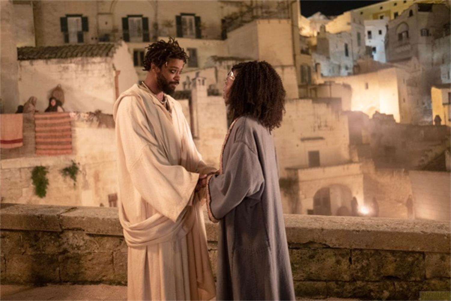 Un uomo e una donna si fronteggiano all'aperto, tenendosi per mano.
