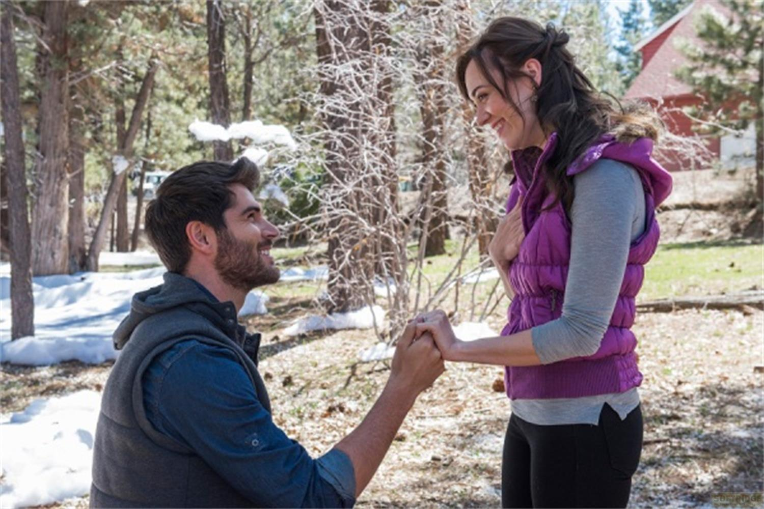 Uomo fa proposta di matrimonio all'aperto, donna si tiene per mano, alberi e neve.