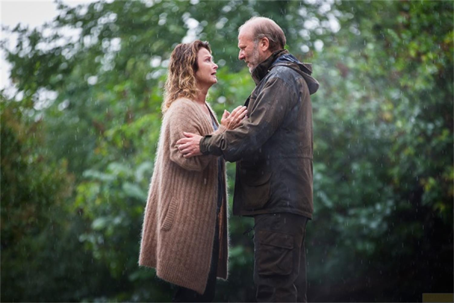 Un homme et une femme se font face sous la pluie. Arbres en arrière-plan.