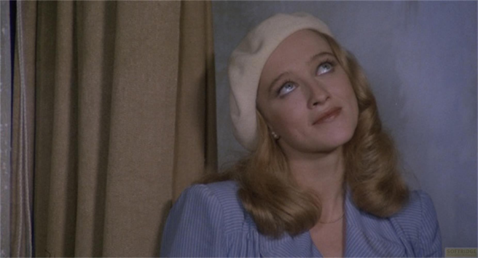 Une femme aux cheveux blonds et au béret blanc regarde vers le haut.