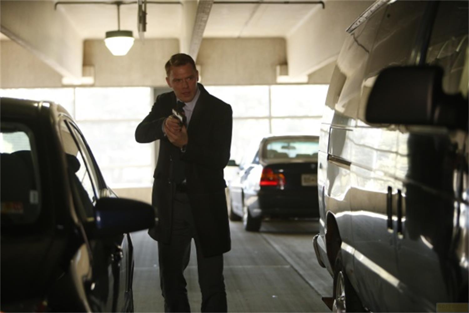 Un homme en costume et pardessus tient une arme, visant dans un parking.