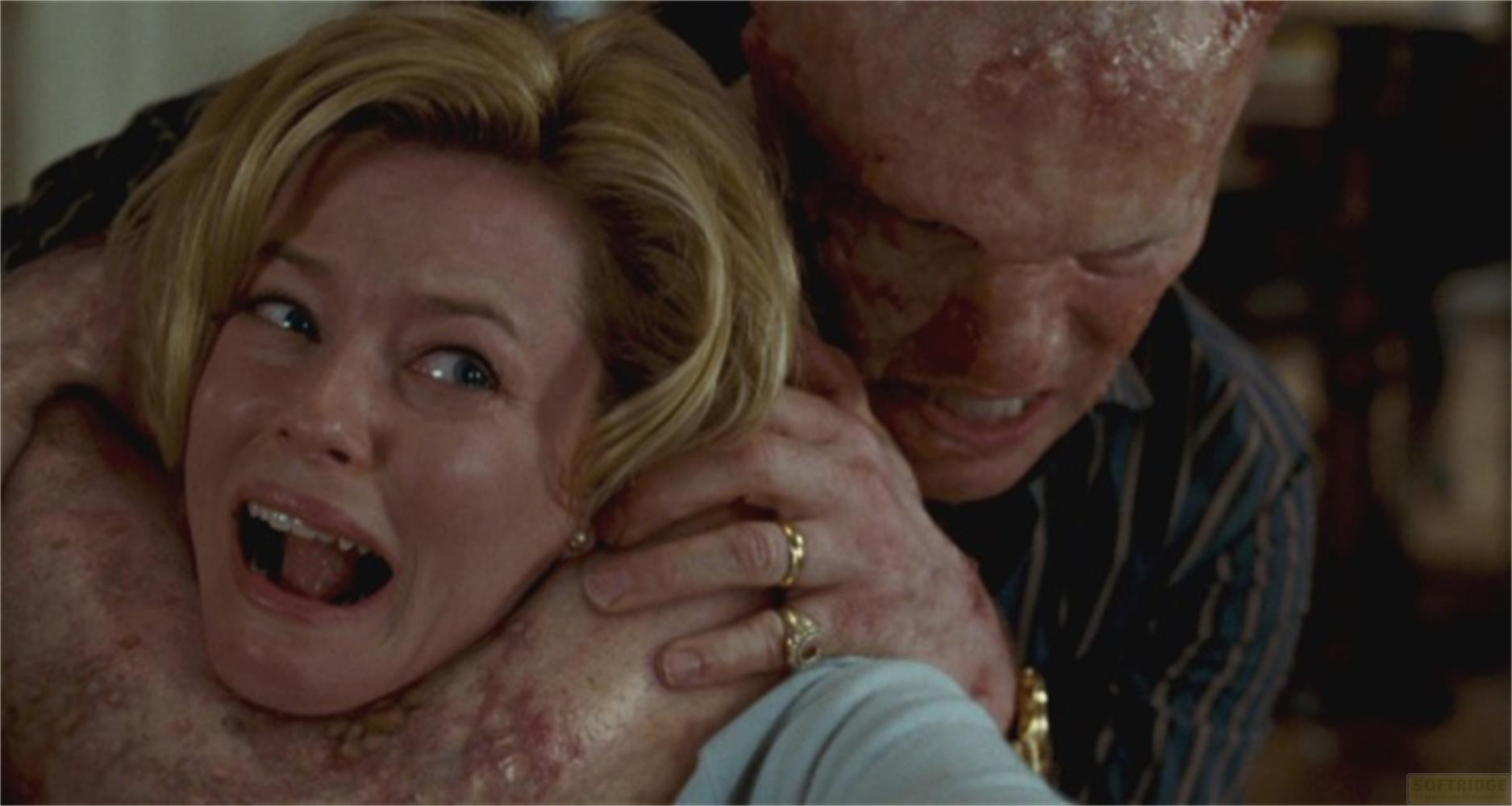Un homme au visage défiguré tient une femme blonde par le cou.