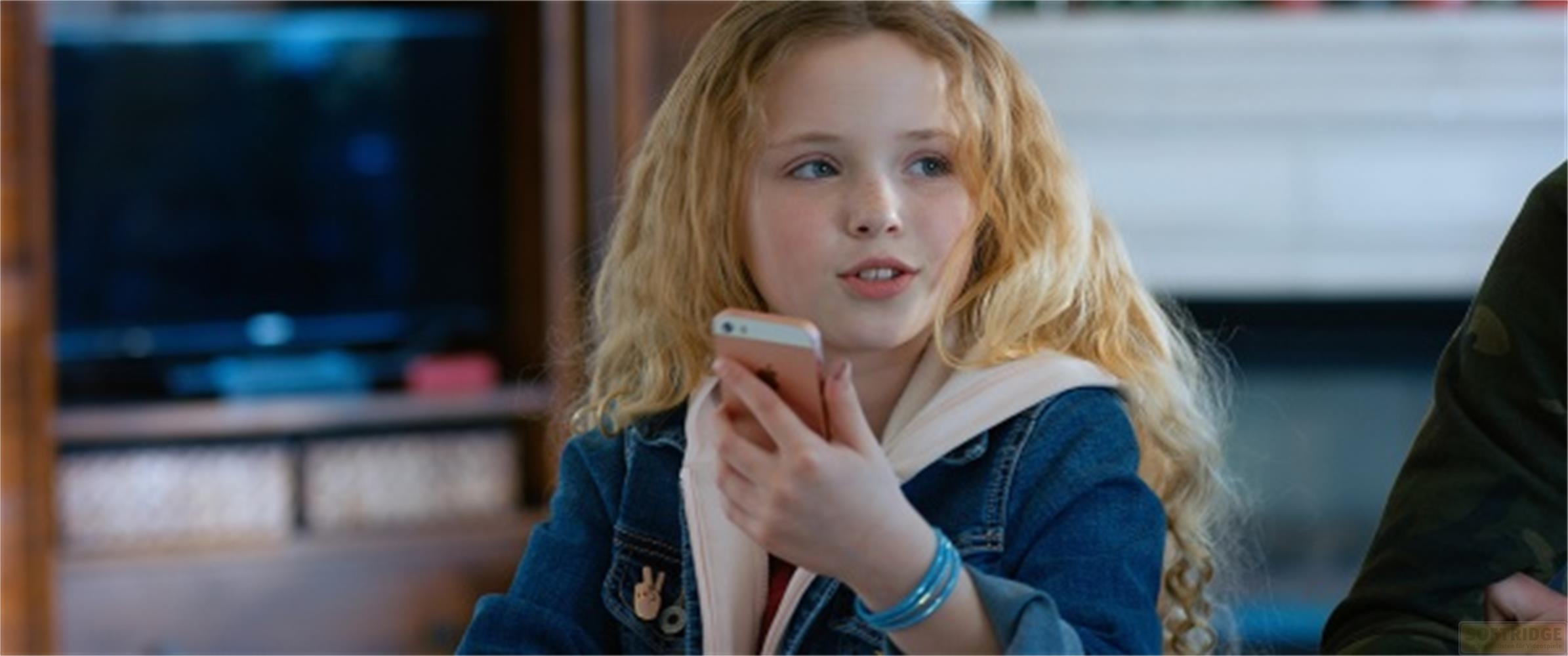 Una bambina dai capelli biondi e ricci tiene in mano uno smartphone rosa.