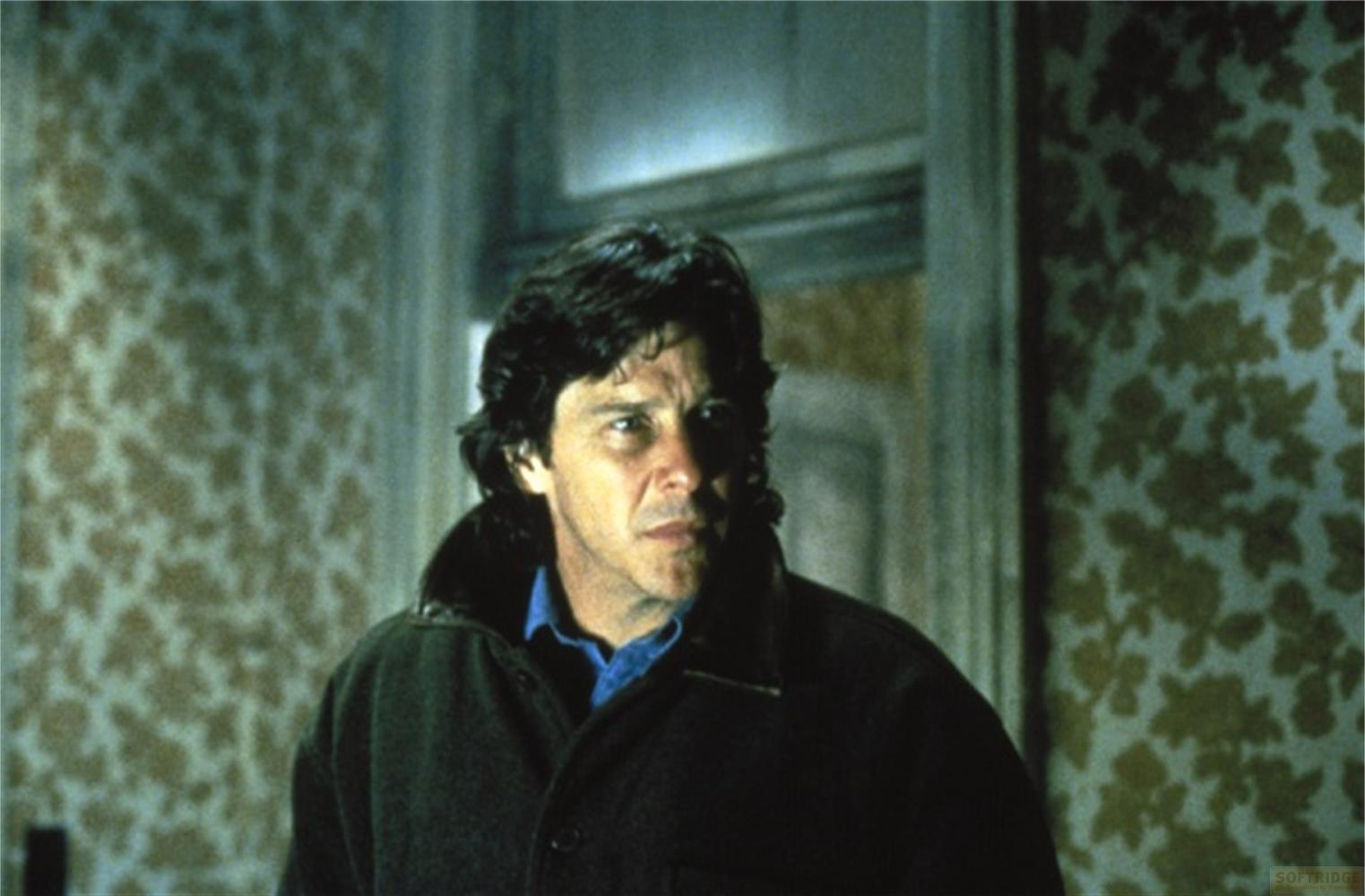 Un homme aux cheveux sombres porte une veste sombre sur une chemise bleue.
