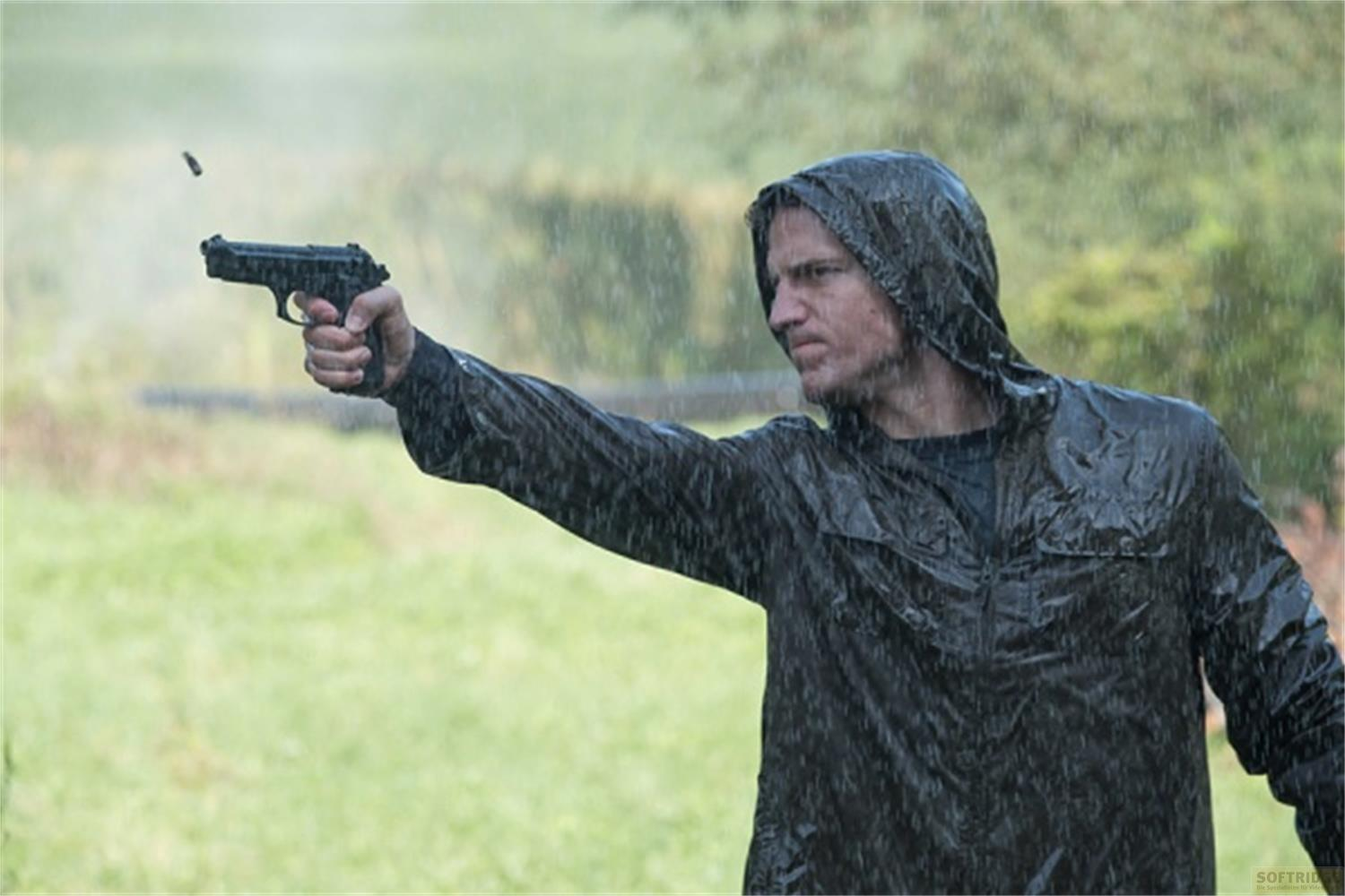 Uomo in impermeabile nero spara con pistola sotto la pioggia.