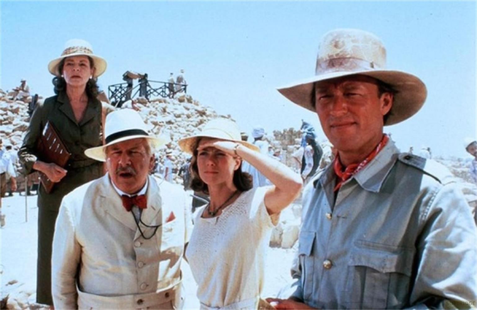 Quattro persone in abiti da deserto davanti a rovine al sole.