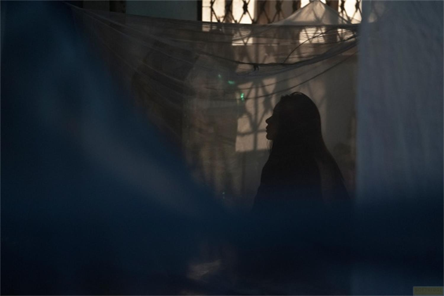 Silhouette di una donna di profilo, in ombra, davanti a una finestra con sbarre.