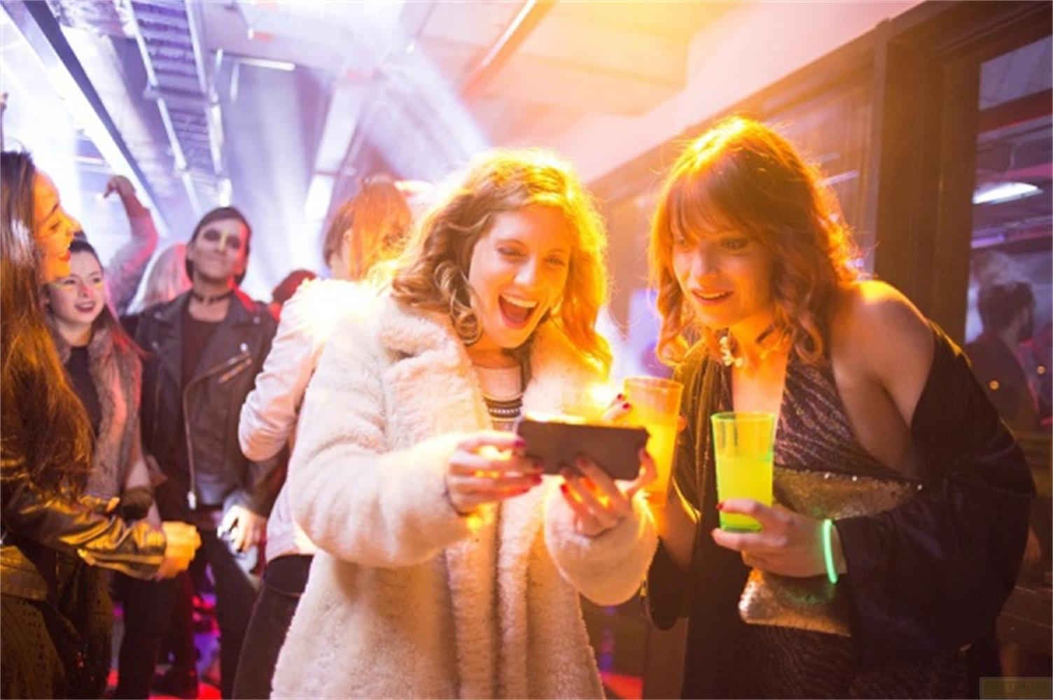 Amici a una festa che tengono telefoni e bevande.