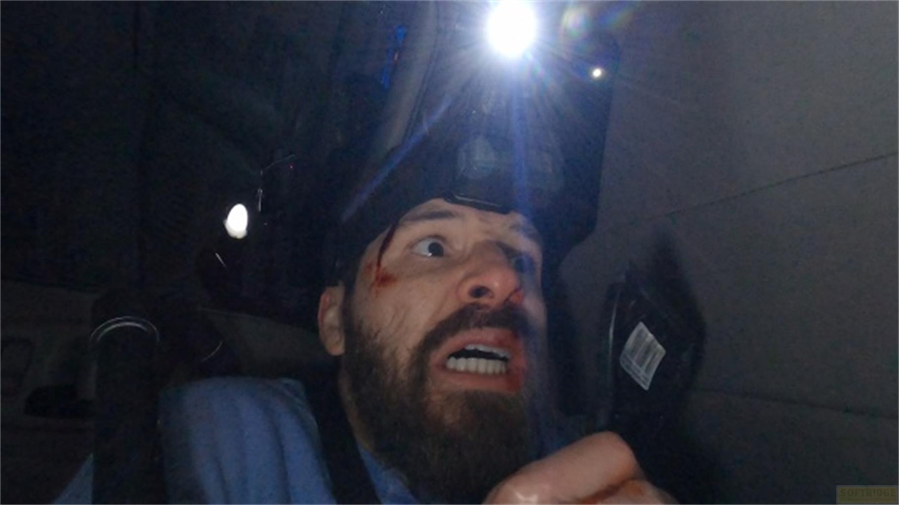 Uomo con lampada frontale, volto insanguinato e barba guarda spaventato.