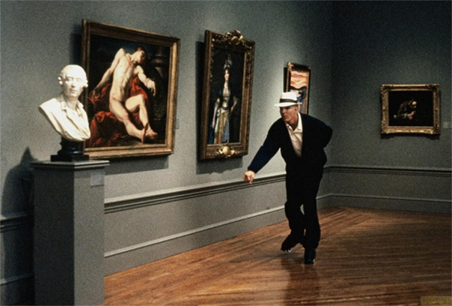 Un uomo con cappello balla in una galleria d'arte davanti a quadri.