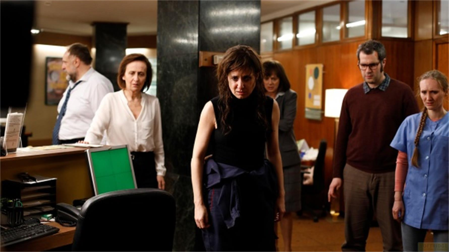 Persone in piedi in un ufficio. Una donna in nero in primo piano, altre dietro.