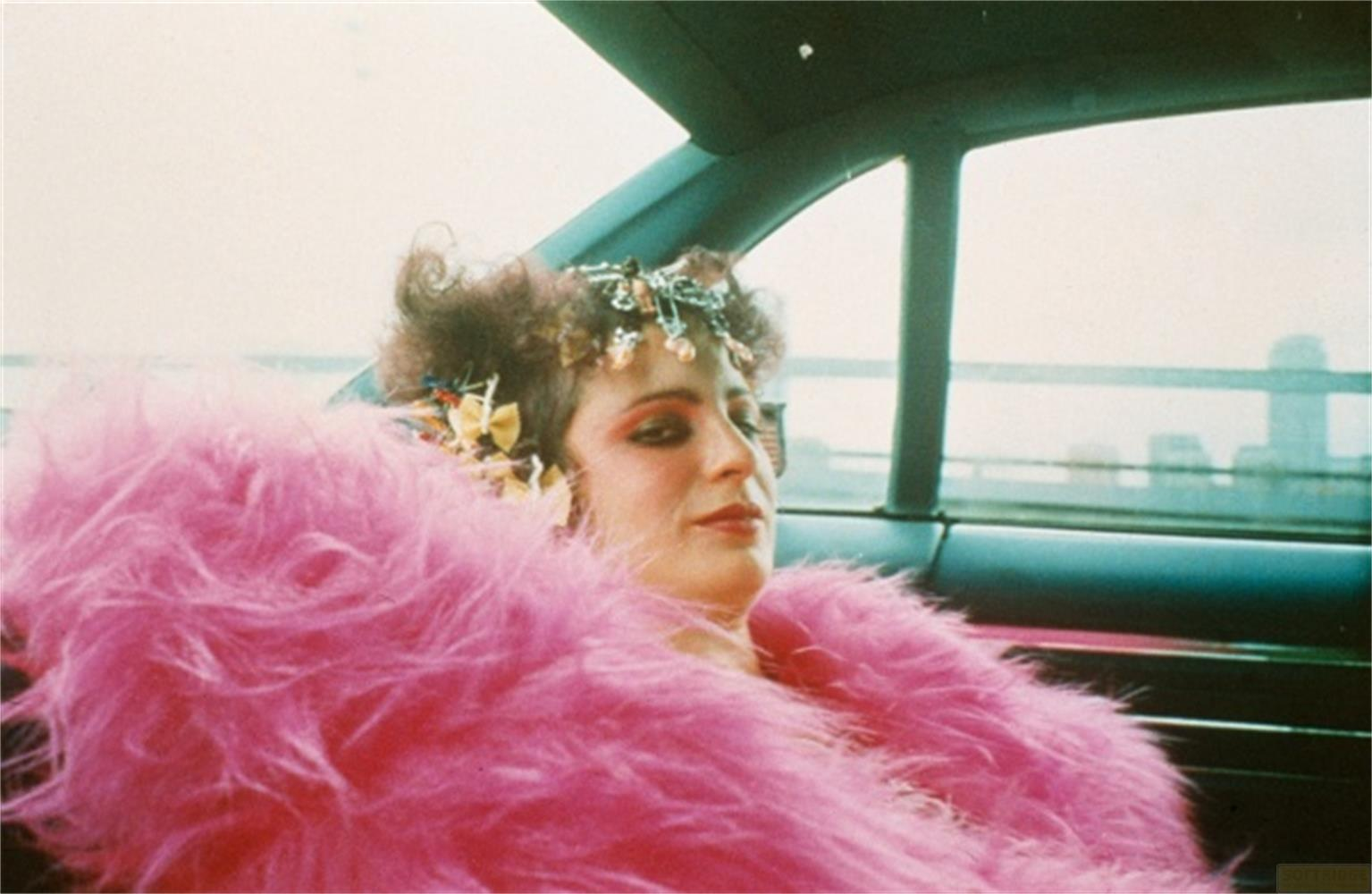 Una donna con boa di piume rosa e copricapo siede in auto.