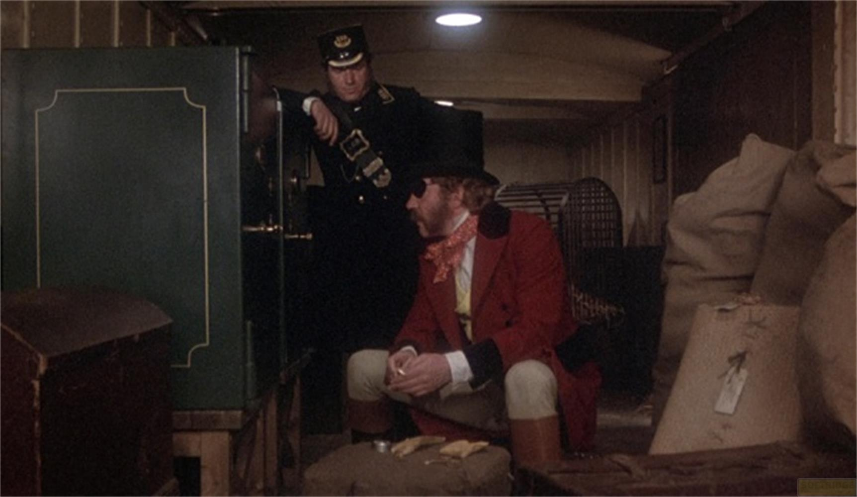 Uomo in uniforme vicino a cassaforte; uomo in cappotto rosso seduto con cappello.